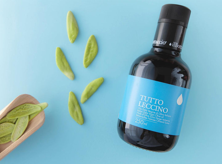 Tutto Leccino Italian extra virgin olive oil bottle and green artisan pasta on blue background, Nostrale Gourmet.